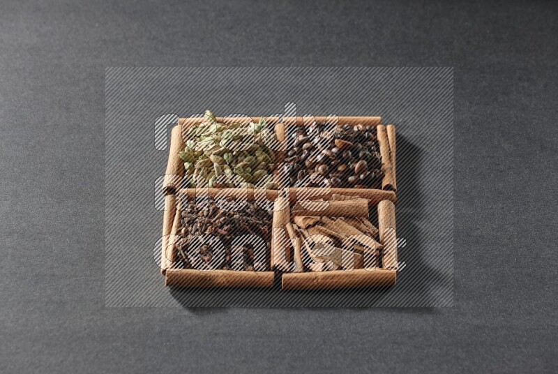 4 squares of cinnamon sticks full of coffee beans, cinnamon, cloves and cardamom on black flooring