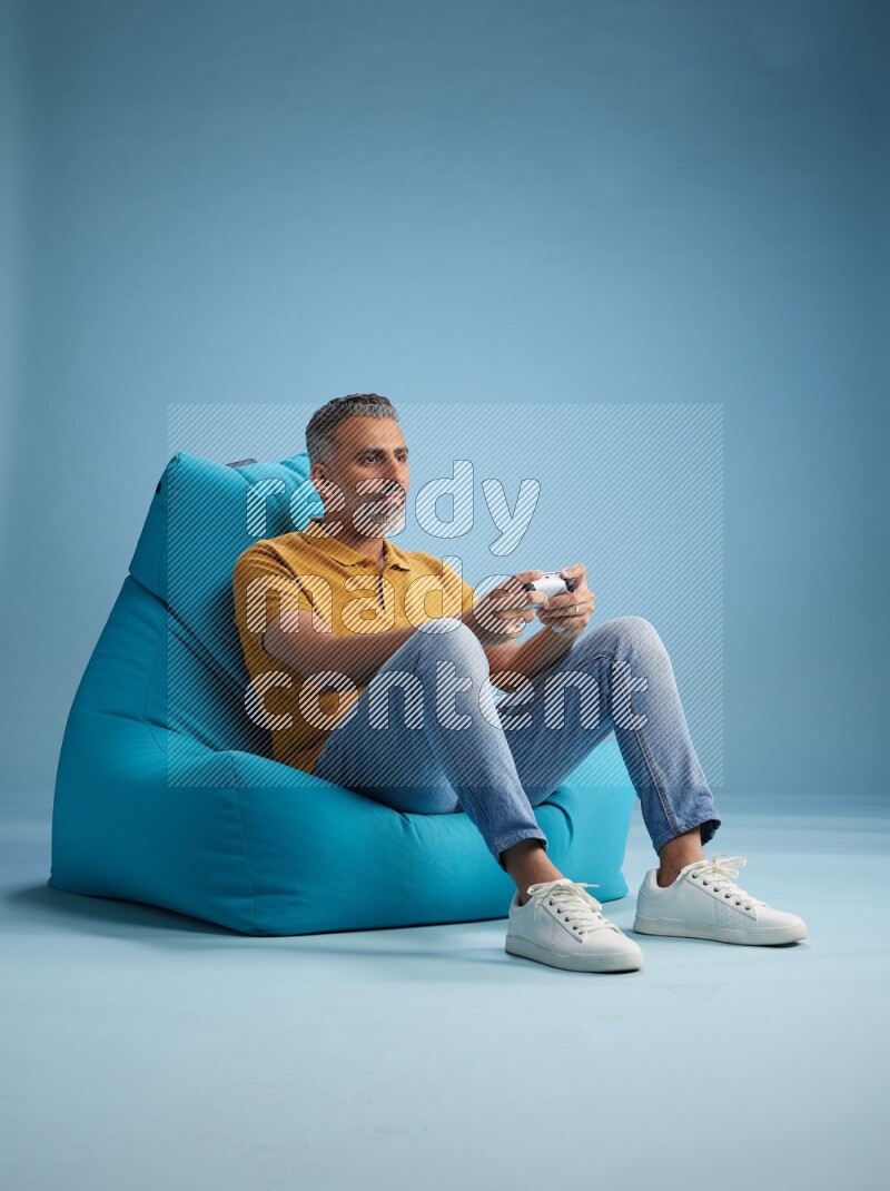 A man sitting on a blue beanbag and gaming with joystick