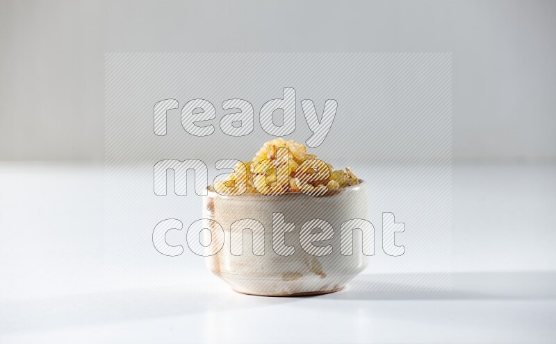 A beige ceramic bowl full of raisins on a white background in different angles