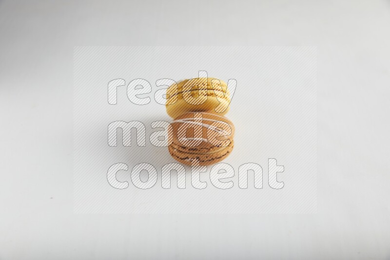 45º Shot of of two assorted Brown Irish Cream, and Yellow Piña Colada macarons on white background
