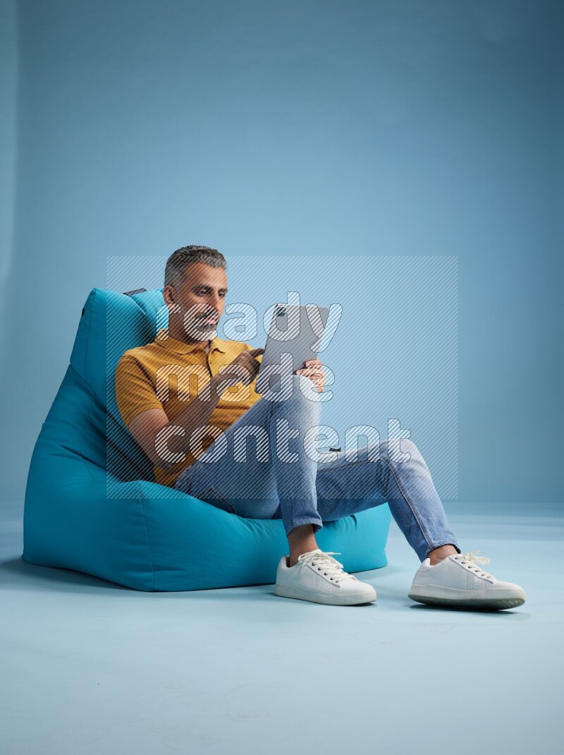 A man sitting on a blue beanbag and working on tablet