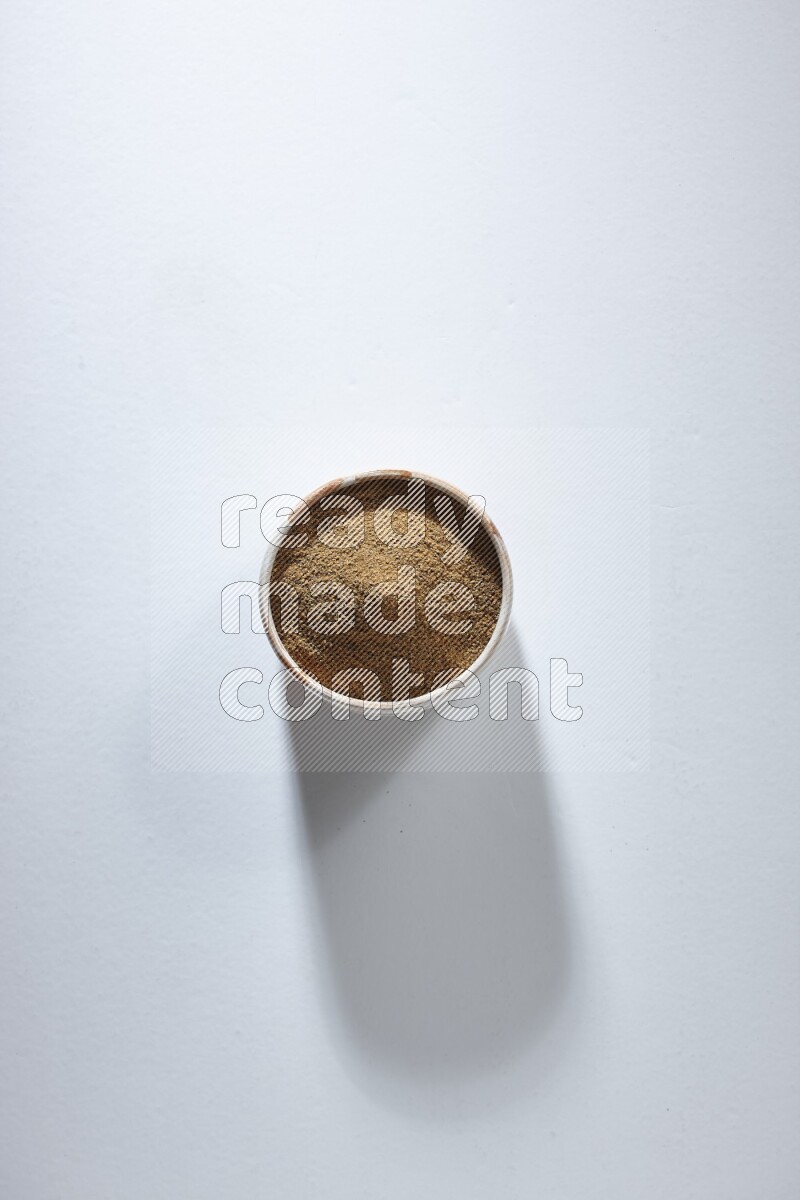 وعاء بيج ممتلئ ببودرة الكمون على خلفية بيضاء