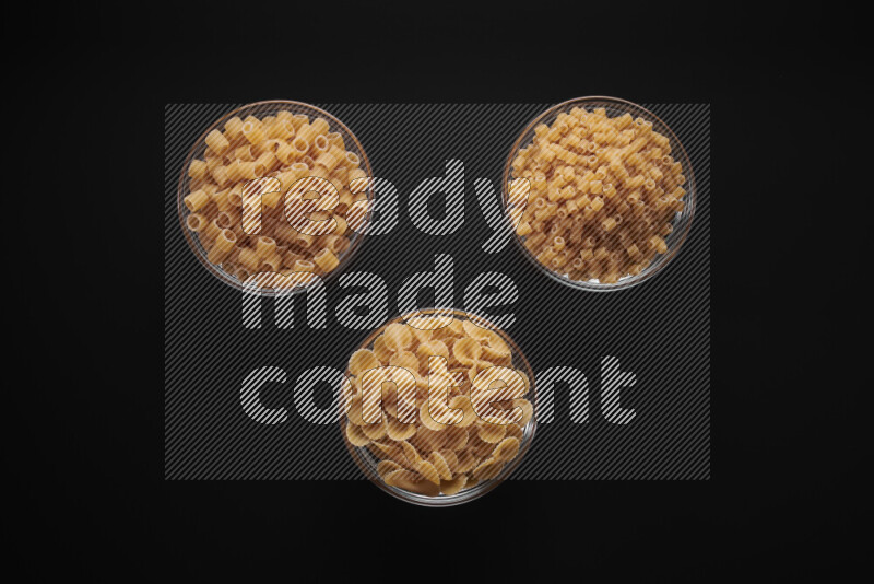 Different pasta types in glass bowls on black background
