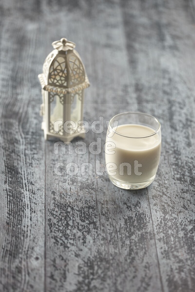 A white lantern with different drinks, dates, nuts, prayer beads and quran on grey wooden background