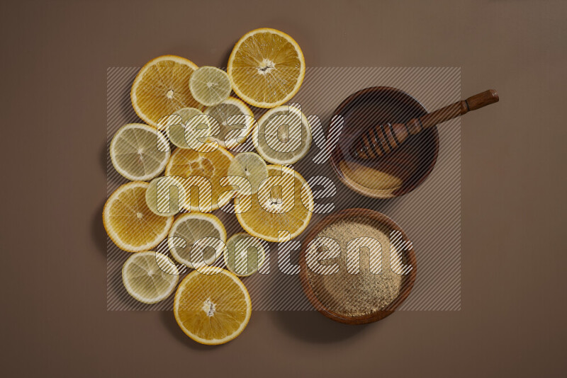 Two bowls full of honey and ground ginger with some of citrus fruits such as lemon and orange on a beige background