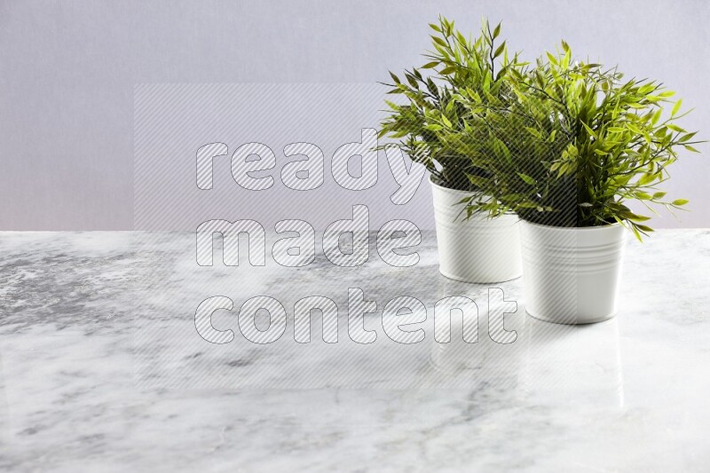 Two green artificial plants in white pot on grey marble background