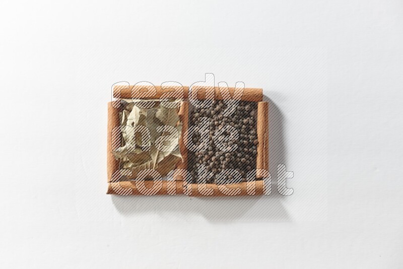 مربعان من أعواد القرفة ممتلئان بحبوب الفلفل الأسود وأوراق الغار علي خلفية بيضاء