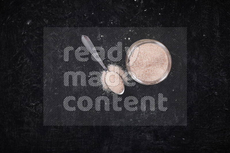 A glass jar full of fine himalayan salt on black background