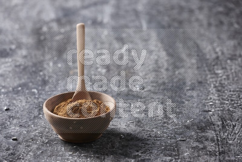 Wooden bowl full of cinnamon powder with a wooden spoon on a textured black background in different angles