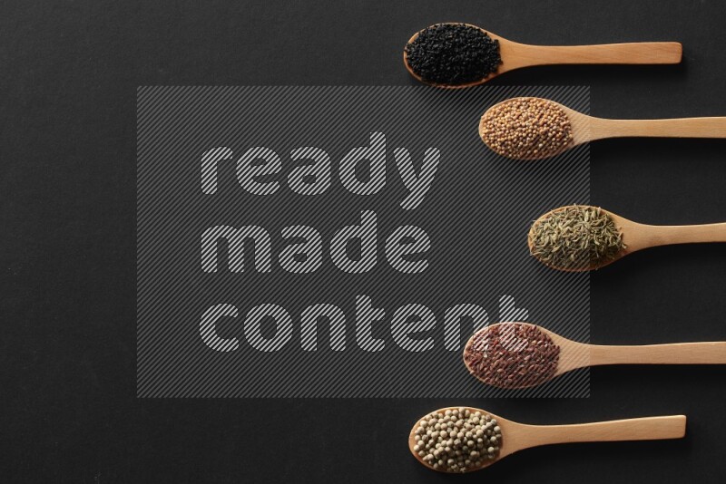 wooden spoons filled with white peppers, mustard seeds, black seeds, garden cress, cumin and flax on black flooring