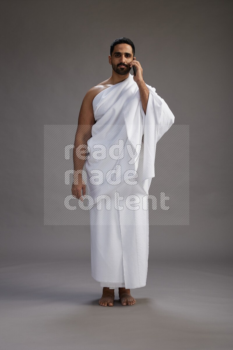A man wearing Ehram Standing talking on phone on gray background