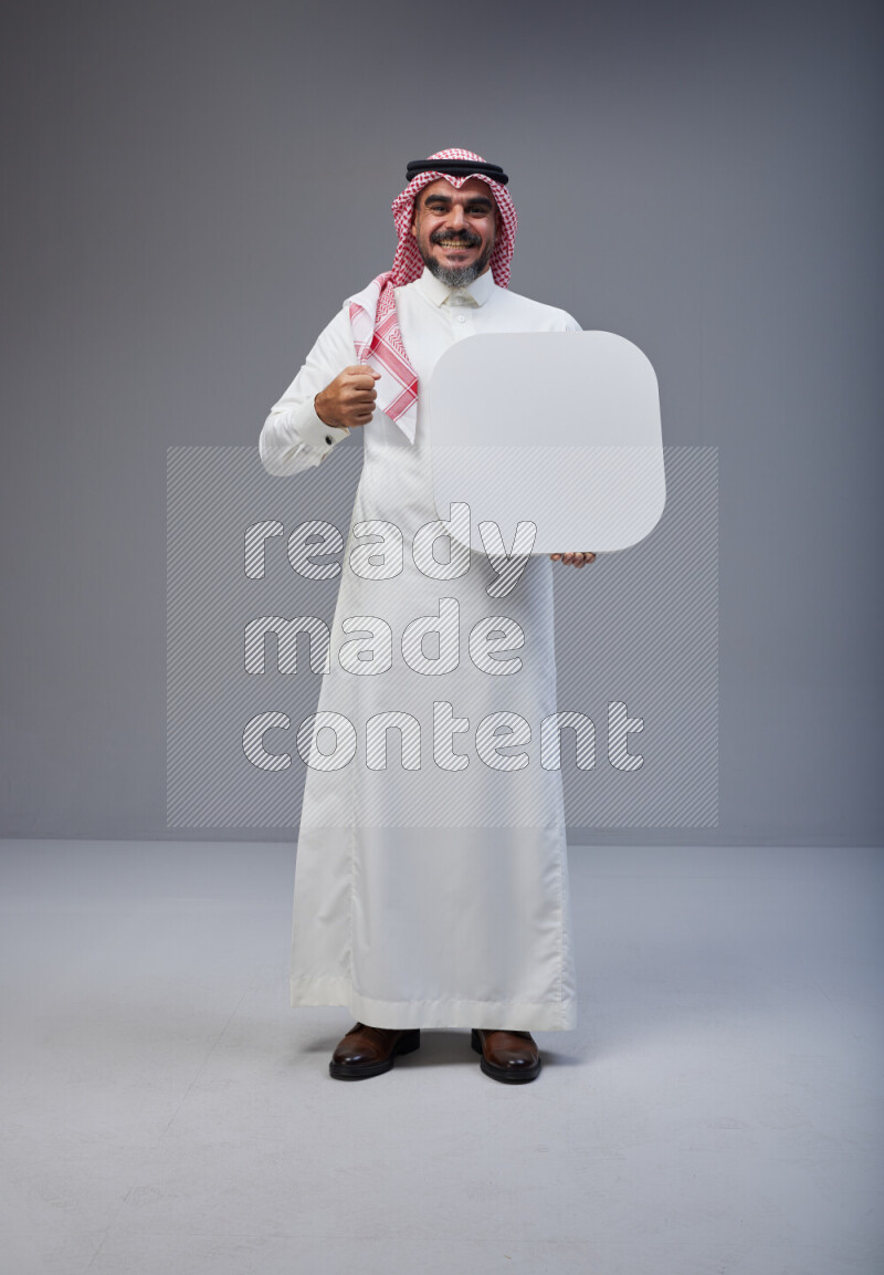 Saudi man Wearing Thob and red Shomag standing holding social media sign on Gray background