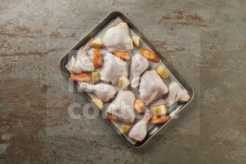 Mixed fresh chicken pieces in an oven tray on a textured rustic background
