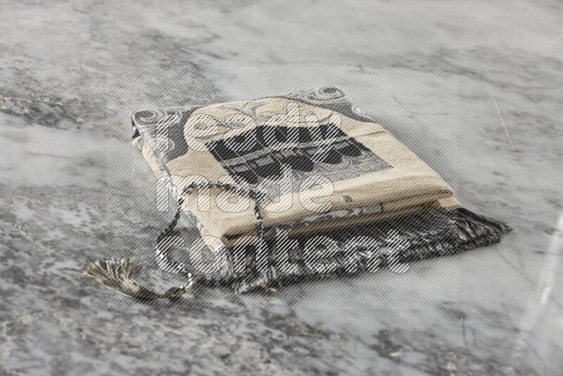 سجادة صلاة مطوية بعناصر مختلفة مثل القرآن الكريم وسبحة الصلاة على خلفية من الرخام باللون الرمادي