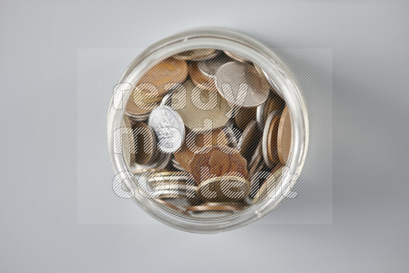 Random old coins in a glass jar on grey background