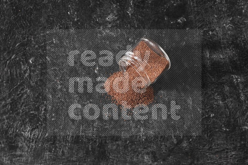 A glass jar full of garden cress seeds flipped and seeds spread out on a textured black flooring