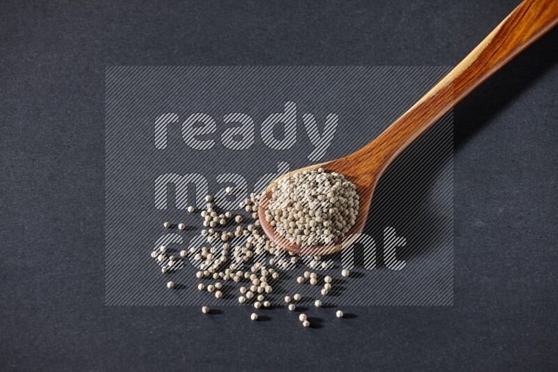 A wooden ladle full of white pepper beads on black flooring