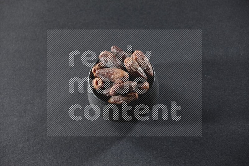 A black pottery bowl full of dried dates on a black background in different angles