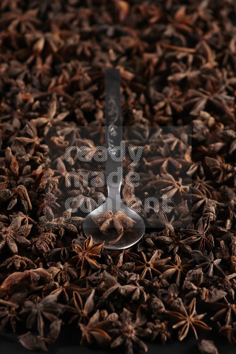 Star Anise in a metal spoon on more stars anise filling the frame on black flooring