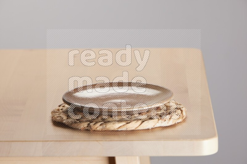 multi-colored pottery Plate placed on a small light colored straw placemat on the edge of wooden table