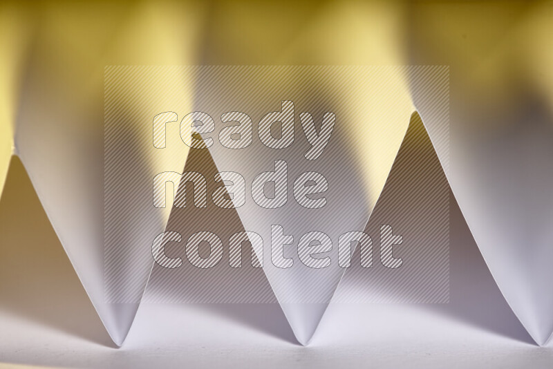 A close-up abstract image showing sharp geometric paper folds in white gradients and warm tones