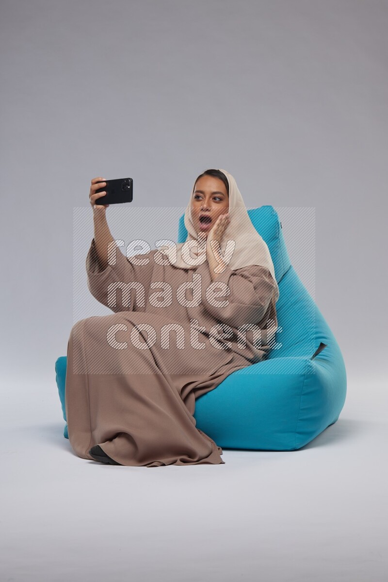 A Saudi woman sitting on a blue beanbag and taking selfie
