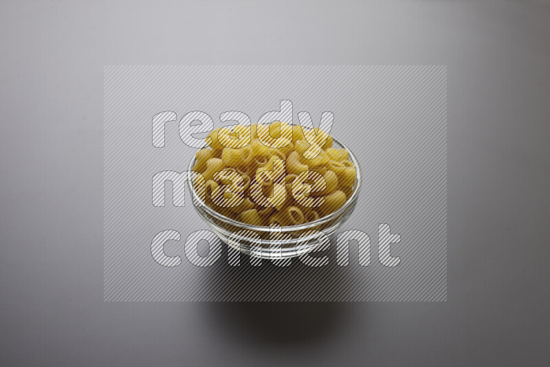 Elbow pasta in a glass bowl on grey background
