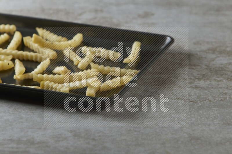 crinkle fries in a black stainless steel rectangle tray on grey textured counter top