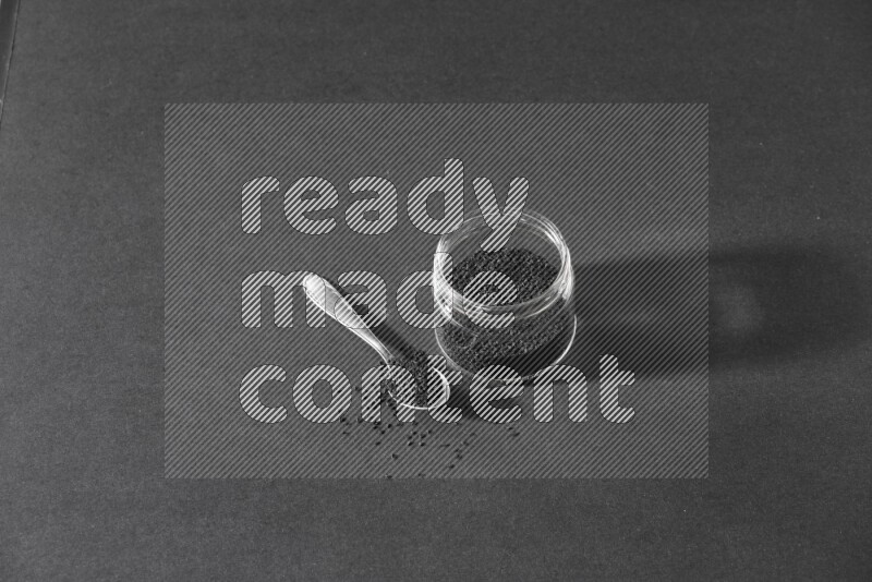 وعاء زجاجي وملعقة معدنية ممتلئان ببذور حبة البركة علي خلفية سوداء