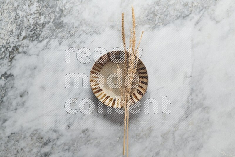 Wheat stalks on multicolored pottery plate on grey marble background