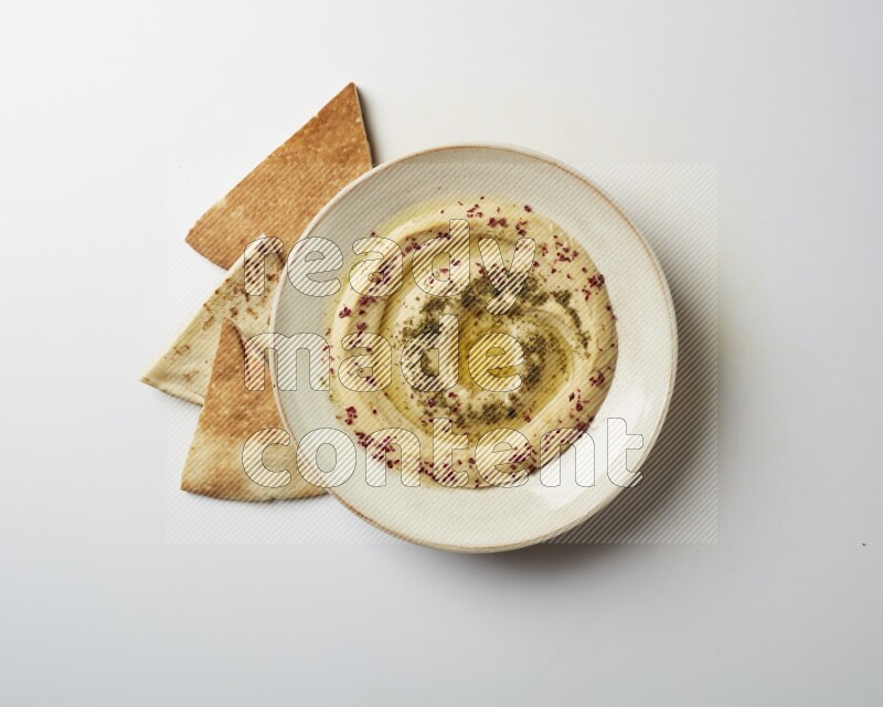 Hummus in a pottry plate garnished with zaatr & sumak on a white background