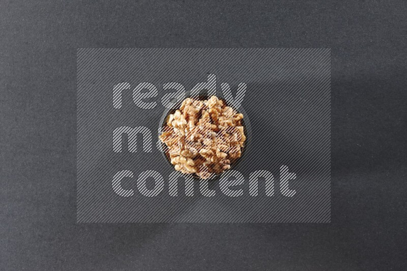 A black pottery bowl full of peeled walnuts on a black background in different angles