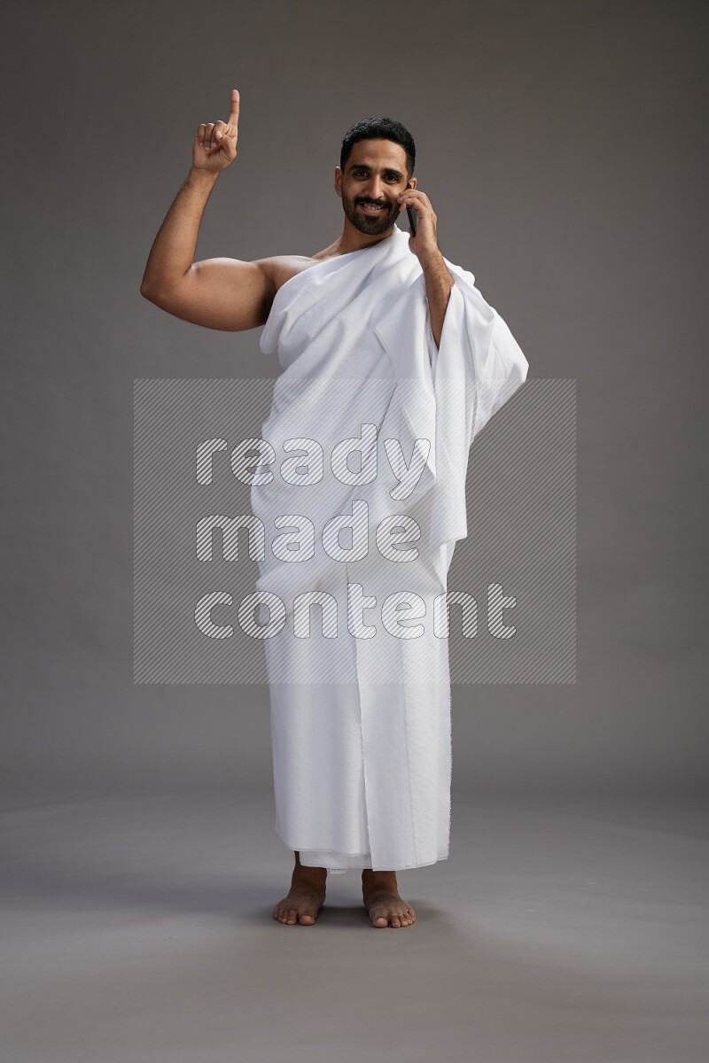 A man wearing Ehram Standing talking on phone on gray background