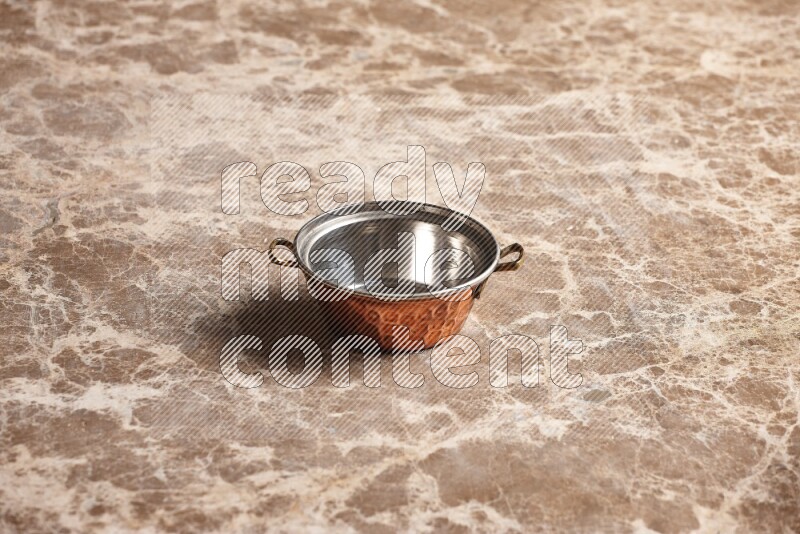 A small copper pot on beige marble background