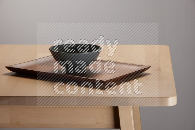 grey bowl placed on a rectangular wooden tray on the edge of wooden table