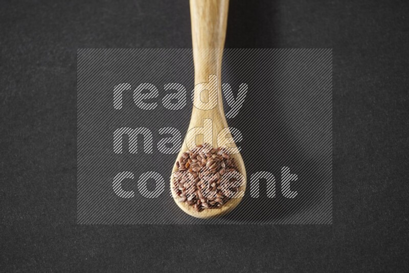 A wooden spoon full of flaxseeds on a black flooring