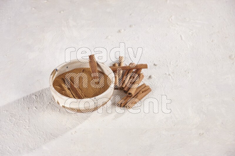 Ceramic bowl full of cinnamon powder with cinnamon sticks on the side on white background