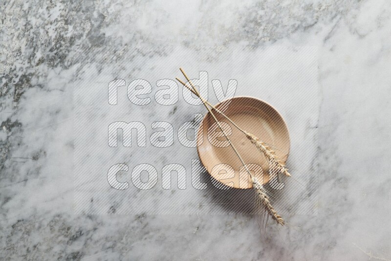 Wheat stalks on beige pottery plate on grey marble background