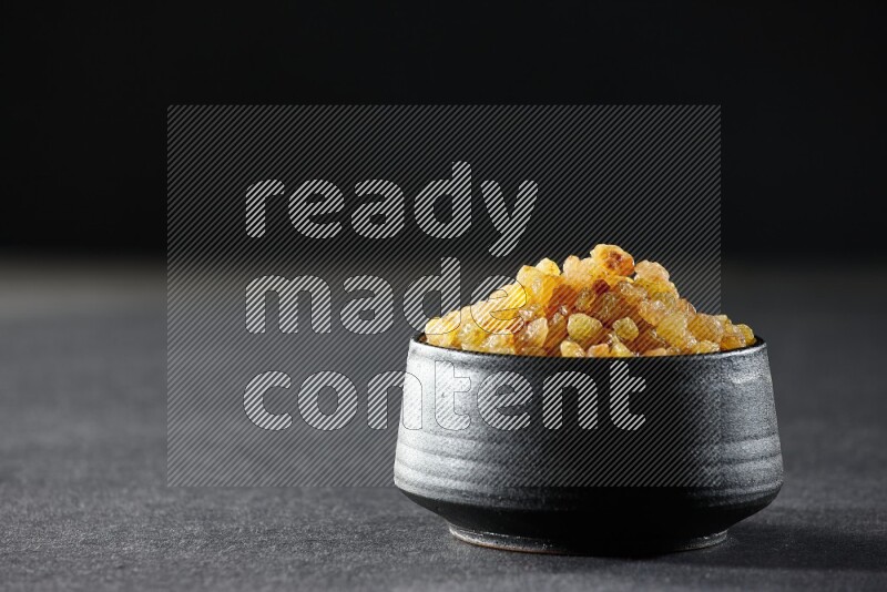 A black pottery bowl full of raisins on a black background in different angles