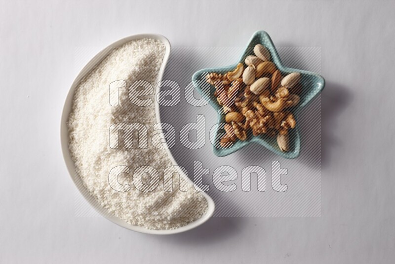Desiccated coconuts in a crescent pottery plate and a star shaped plate with mixed nuts on white background