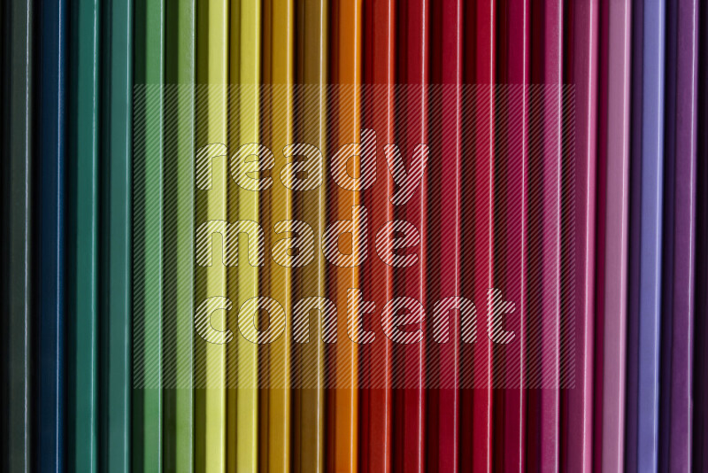A collection of colored pencils arranged showcasing a gradient of different hues on grey background