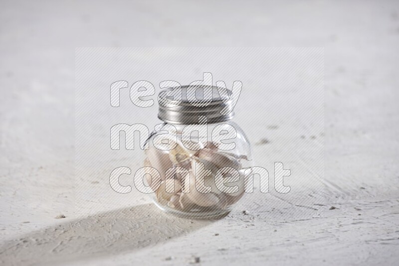 A glass spice jar full of garlic cloves on a textured white flooring