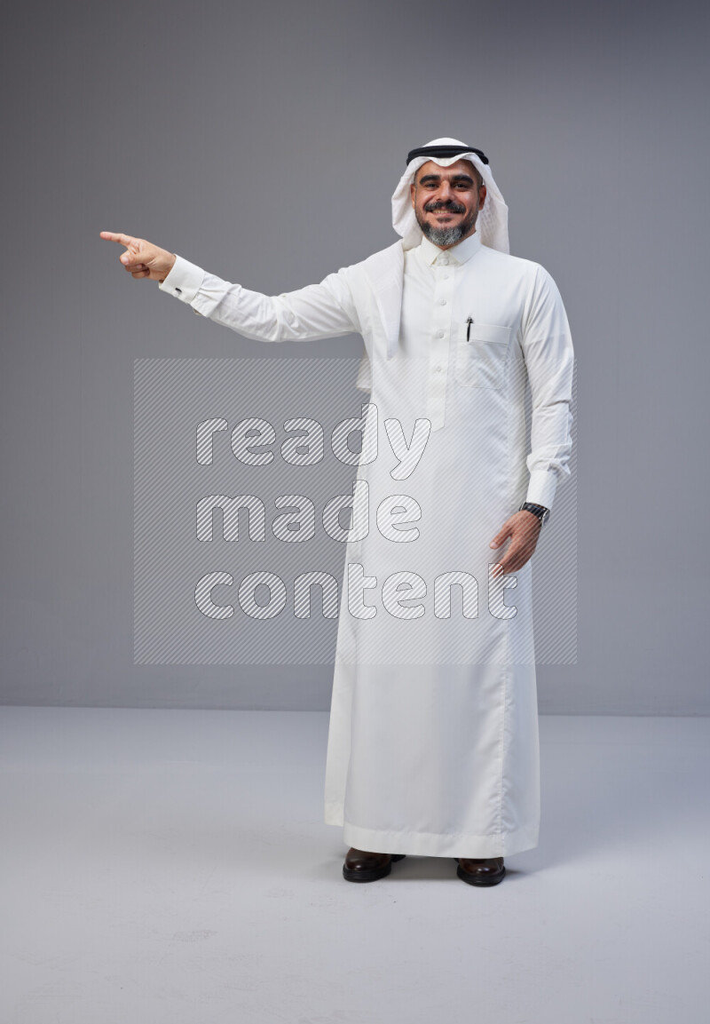 Saudi man Wearing Thob and white Shomag standing interacting with the camera on Gray background