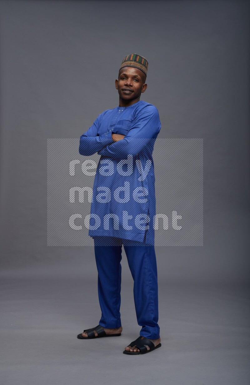 Man wearing Nigerian outfit standing with crossed arms on gray background