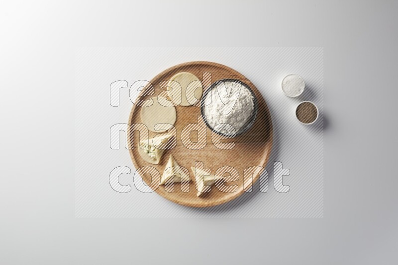 two closed sambosas and one open sambosa filled with cheese while flour, salt, and black pepper aside in a wooden dish on a white background