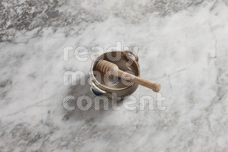 Multicolored pottery bowl with wooden honey dipper in it on grey marble background