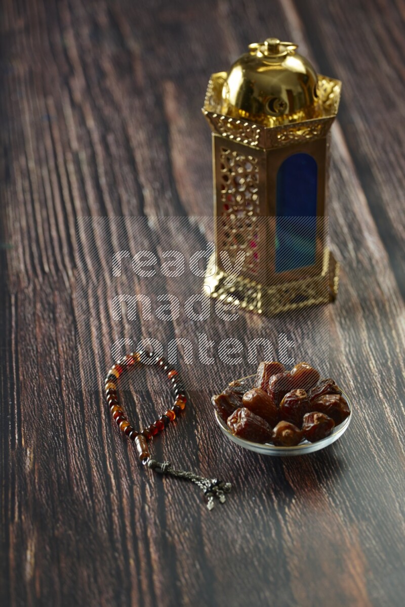 A golden lantern with different drinks, dates, nuts, prayer beads and quran on brown wooden background
