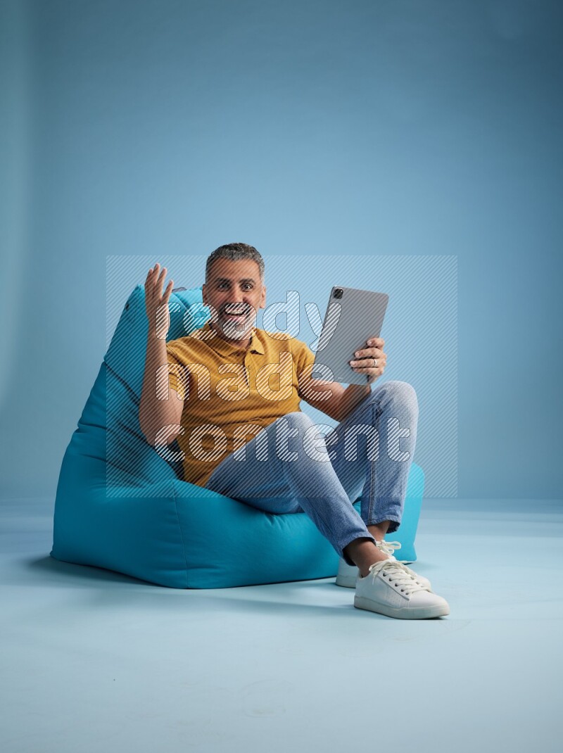 A man sitting on a blue beanbag and working on tablet