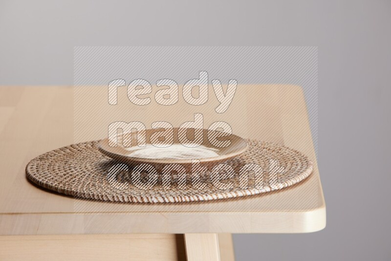 multi-colored pottery Plate placed on a big light colored straw placemat on the edge of wooden table