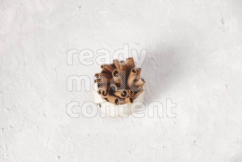Cinnamon sticks in a beige bowl on a white background